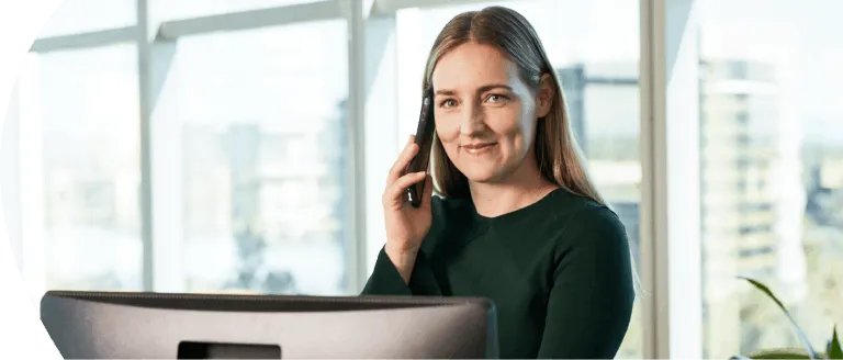 Person sitting in front of computer, talking on a phone.